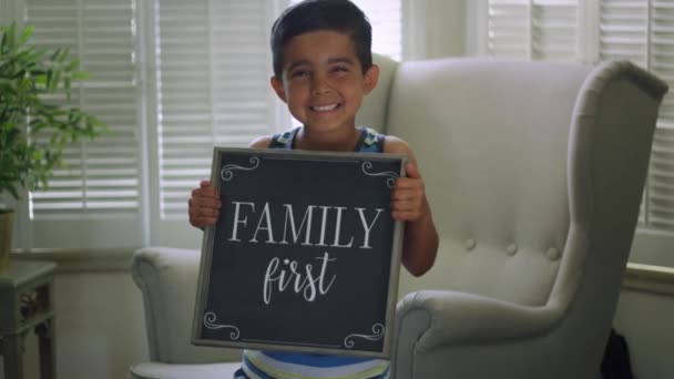 Slow motion van jongen houdt van teken dat "Family First zegt" als hij naar camera glimlacht — Stockvideo