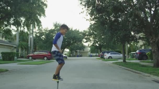 Movimiento lento de un niño saltando sobre un palo de pogo en un barrio rural — Vídeos de Stock