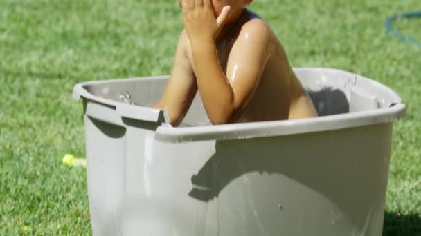 Медленное движение маленького мальчика внутри пластиковой корзины, наполненной водой — стоковое видео