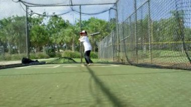 Ağır çekim vurmak için beyzbol Park'ta kafes vuruş, sopasını tutan ve iyi bir top için bekleyen içinde küçük bir çocuk
