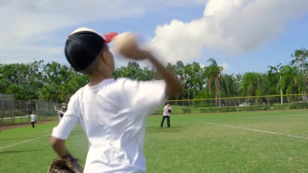 昼間のスロー モーション他の子供に野球の練習中にボールを投げる少年の後ろからのショットになります 練習だけでなく後ろに他の子供たちを見ることができます — ストック動画