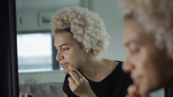 Mulher transgênero aplicando maquiagem enquanto olha para si mesma em um espelho compacto — Vídeo de Stock