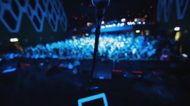 Nahaufnahme eines Mikrofons auf der Bühne vor einem Konzert mit Menschen, die davor warten — Stockvideo