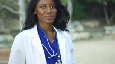 Beyaz önlük giyen ve kameraya gülümseyen güzel siyah kadın doktor, ağır çekim