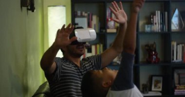 Ağır çekim bir Vr mezartaşı ile oynarken bir kanepede oturan babası izlerken çocuk