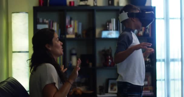 Tournage au ralenti de la mère et du fils à la maison. Le fils joue avec un casque de réalité virtuelle pendant que sa mère regarde et sourit .