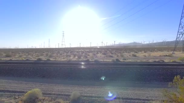 カリフォルニアのフィールドで列車の線路のパンショットは 電気塔と風車で地域の航空写真を表示します — ストック動画