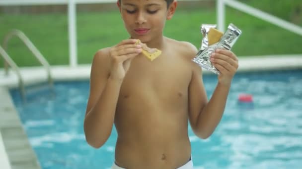 수영장 앞에서 카메라에 미소를 짓는 동안 먹는 어린 소년의 슬로우 모션 — 비디오