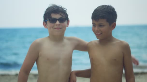 Cámara lenta de dos niños abrazándose y sonriendo a la cámara en la playa — Vídeos de Stock