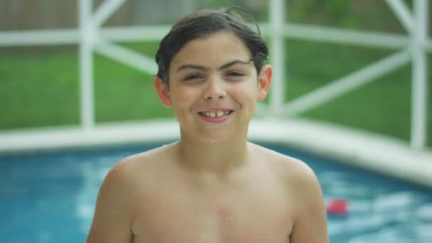 Симпатичний хлопчик посміхається на камеру, стоячи перед басейном у купальнику — стокове відео