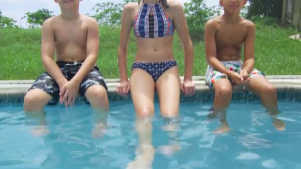 Два мальчика и девочка сидят у бассейна и улыбаются в камеру. — стоковое видео