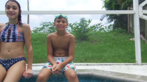 Дети сидят у бассейна, смотрят в камеру и улыбаются. — стоковое видео
