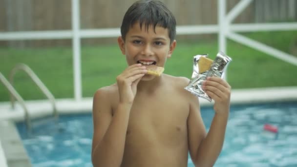 Slow Motion av en söt pojke äta och leende framför en swimmingpool — Stockvideo