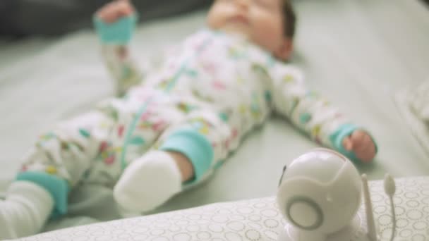 Дитина рухається в ліжку поруч з дитячим монітором — стокове відео
