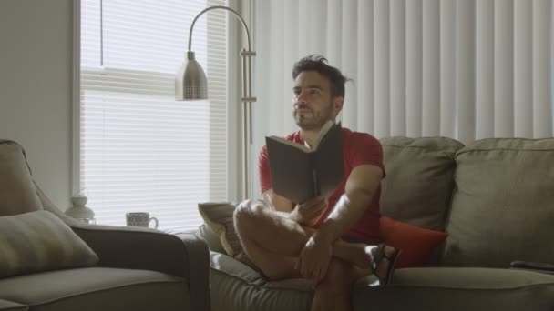 Zeitlupe eines Mannes, der ein Buch in der Hand hält, während er nachdenklich aufblickt — Stockvideo
