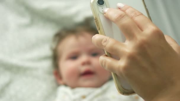 Lassú mozgás baba feküdt az ágyban, és mosolyogva a mobiltelefonján — Stock videók
