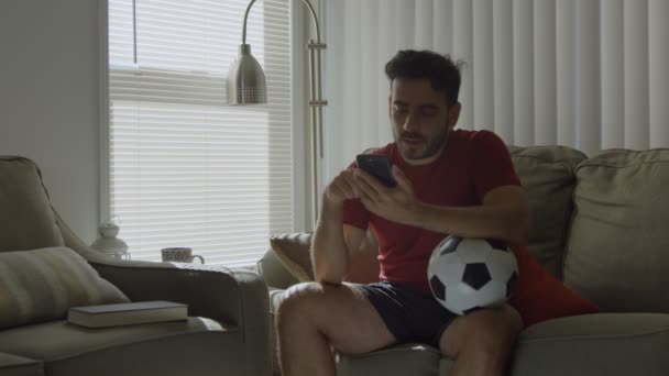 Tifoso di calcio che controlla i social media mentre tiene il pallone da calcio a casa — Video Stock