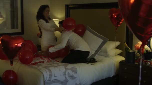 Feliz recién casados saltando en la cama con globos y pétalos de rosa — Vídeo de stock