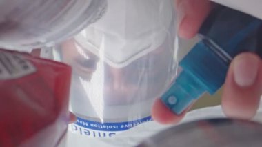 Yüzü maskeli bir adam alışverişe çıkmadan önce elleri ve poşetleri sterilize ediyor. 