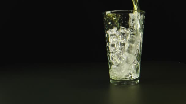Makro ujęcie wody wylewanej na szklankę z lodem, czarne tło. — Wideo stockowe