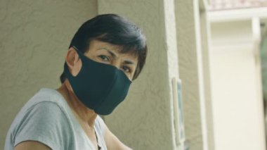 Koruyucu yüz maskeli yaşlı kadın ciddi bir yüzle kameraya bakıyor.