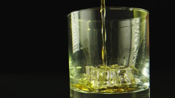 Makro skjuten i slow motion av en drink som hälls på ett glas. Bakgrunden är svart. — Stockvideo