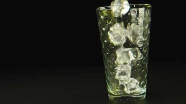 Makro zbliżenie strzał lodu spada na szklankę. Tło jest czarne. — Wideo stockowe