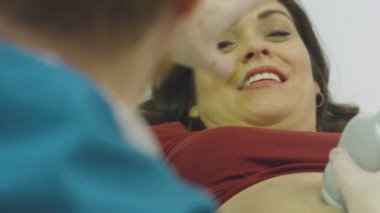 Doktor ultrason çekilirken hamile bir kadınla konuşuyor.