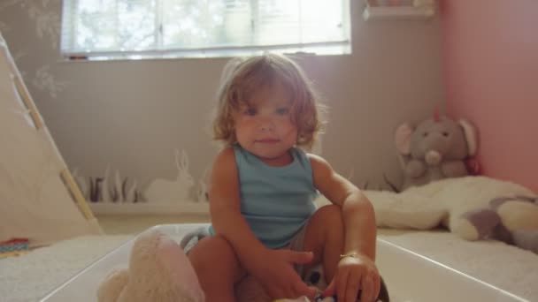 Little girl looking towards camera and smiling while sitting in her room — Stock Video