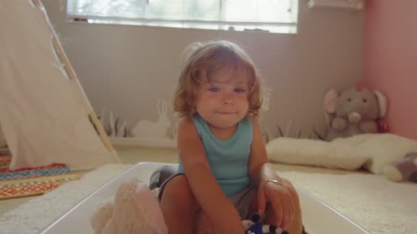 Klein meisje kijkt naar camera, glimlacht en dekt lens met de hand — Stockvideo