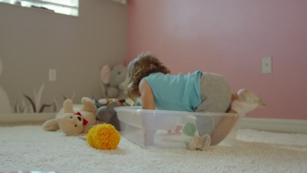 Küçük bir kızın oyuncaklarla plastik bir kutunun içine girmesi. — Stok video