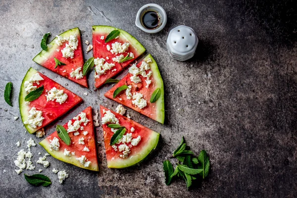 Fresh watermelon pizza salad with feta cheese, mint, salt and oil on stone background.