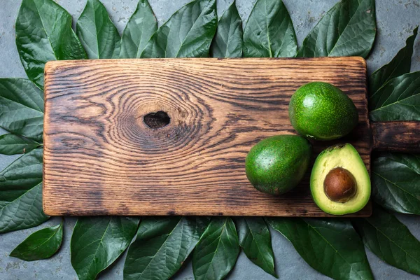 新鮮なアボカド アボカドの木葉と木製のまな板を持つ食品背景 収穫の概念 ワカモレの材料 健康的な脂肪 オメガ アボカドの半分 平面図です コピー スペース — ストック写真
