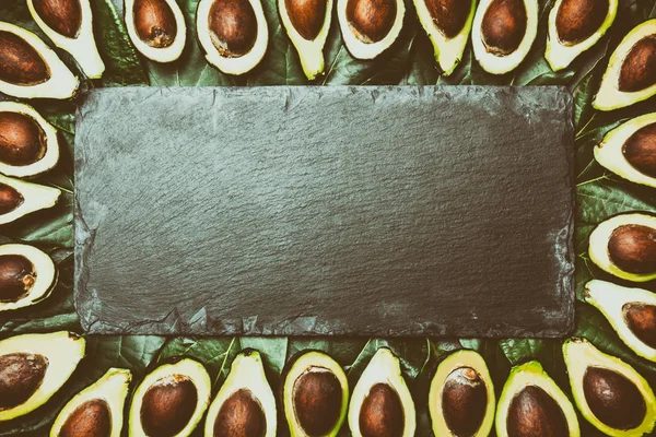 Avocado. Frame made from avocado palta and avocado tree leaves slate board. Guacamole ingredients. Healthy fat, omega 3. Half of avocado. Top view. Copy space