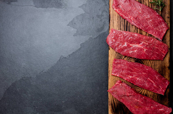 Fresh raw meat beef steaks. Beef tenderloin on wooden board, spices, herbs, oil on slate gray background. Food background with copy space.