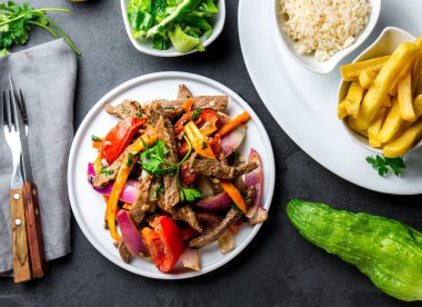 Perulu çanak Lomo saltado - Dana Bonfile mor soğan, sarı biber, domates ile beyaz tabak kızarmış patates ve pilav ile servis. Üstten görünüm