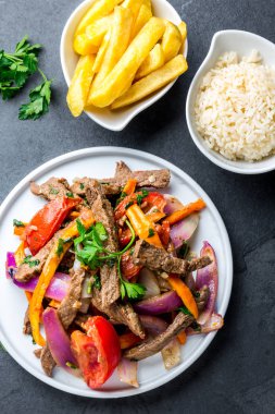 Perulu çanak Lomo saltado - Dana Bonfile mor soğan, sarı biber, domates ile beyaz tabak kızarmış patates ve pilav ile servis. Üstten görünüm
