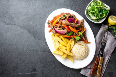 Perulu çanak Lomo saltado - Dana Bonfile mor soğan, sarı biber, domates ile beyaz tabak kızarmış patates ve pilav ile servis. Üstten görünüm