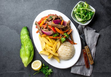 Perulu çanak Lomo saltado - Dana Bonfile mor soğan, sarı biber, domates ile beyaz tabak kızarmış patates ve pilav ile servis. Üstten görünüm