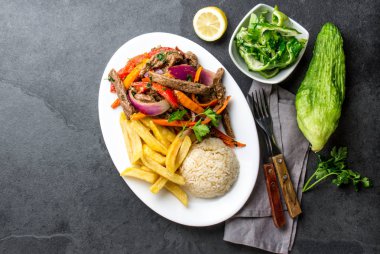Perulu çanak Lomo saltado - Dana Bonfile mor soğan, sarı biber, domates ile beyaz tabak kızarmış patates ve pilav ile servis. Üstten görünüm