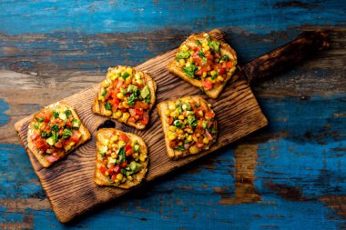 Meksikalı Latin Amerikan tarzı açık sandviçler. Vejetaryen tost ile Mısır, avokado, domates ahşap tahta üzerinde. Rustik ahşap mavi arka plan. Üstten görünüm.