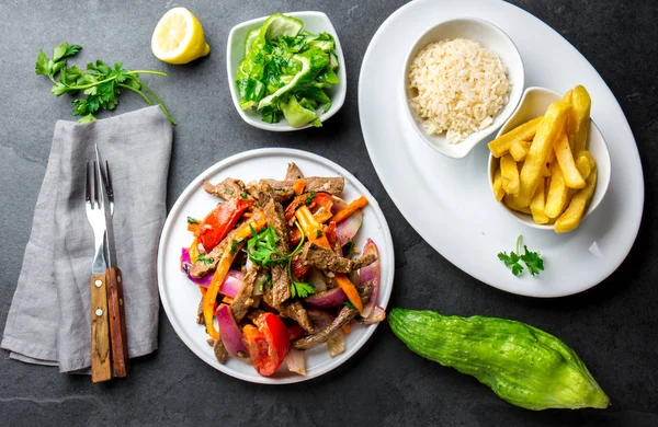 Perulu çanak Lomo saltado - Dana Bonfile mor soğan, sarı biber, domates ile beyaz tabak kızarmış patates ve pilav ile servis. Üstten görünüm