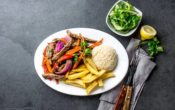 Perulu çanak Lomo saltado - Dana Bonfile mor soğan, sarı biber, domates ile beyaz tabak kızarmış patates ve pilav ile servis. Üstten görünüm