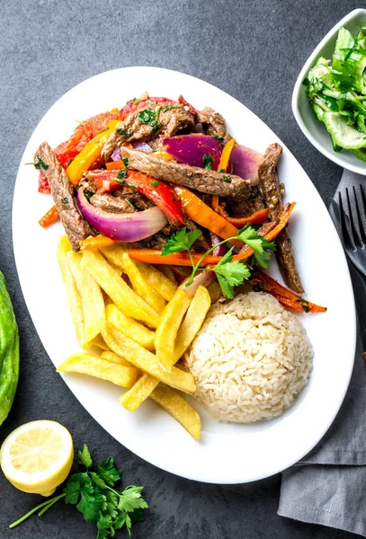 Perulu çanak Lomo saltado - Dana Bonfile mor soğan, sarı biber, domates ile beyaz tabak kızarmış patates ve pilav ile servis. Üstten görünüm