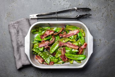 Metal pot, arduvaz arka planda pastırmalı kızarmış bezelye pod. Üstten görünüm