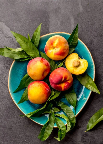 Fresh ripe peach with peach tree leaves on blue plate, top view.