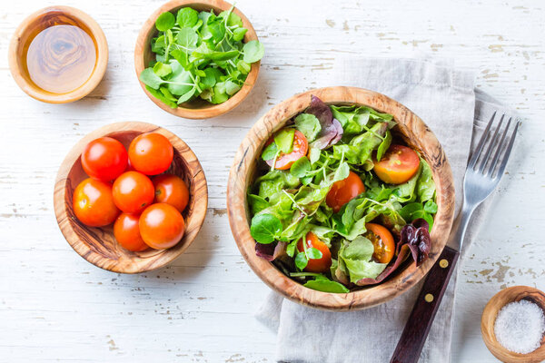 Вегетарианский салат с салатом и помидорами в оливковой деревянной миске на заднем плане
