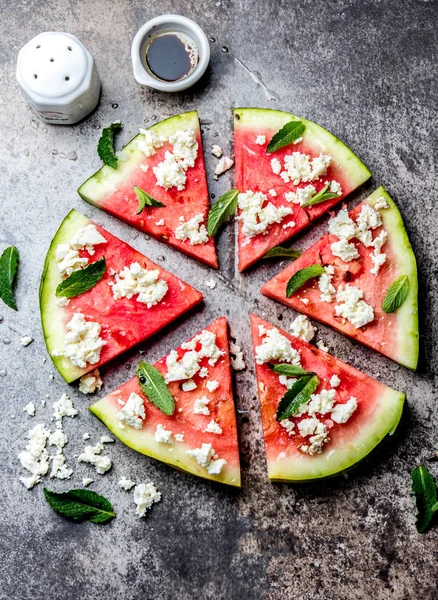 Fresh watermelon pizza salad with feta cheese, mint, salt and oil on stone background.