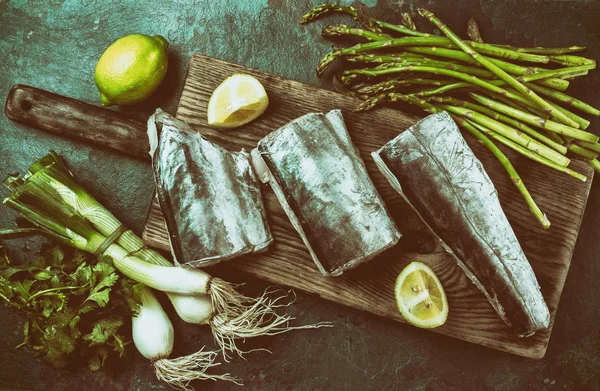 Food background with raw sawfish asparagus, lemon and herbs. Top view. Toned.
