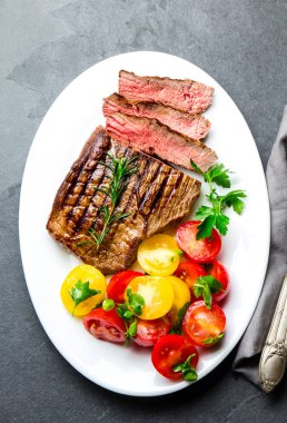 Domates salatası ve patates topları ile beyaz tabakta Orta nadir ızgara sığır eti biftek dilimlenmiş. Barbekü, Barbekü et Dana Bonfile. Üstten görünüm, arduvaz arka plan, kopya alanı.